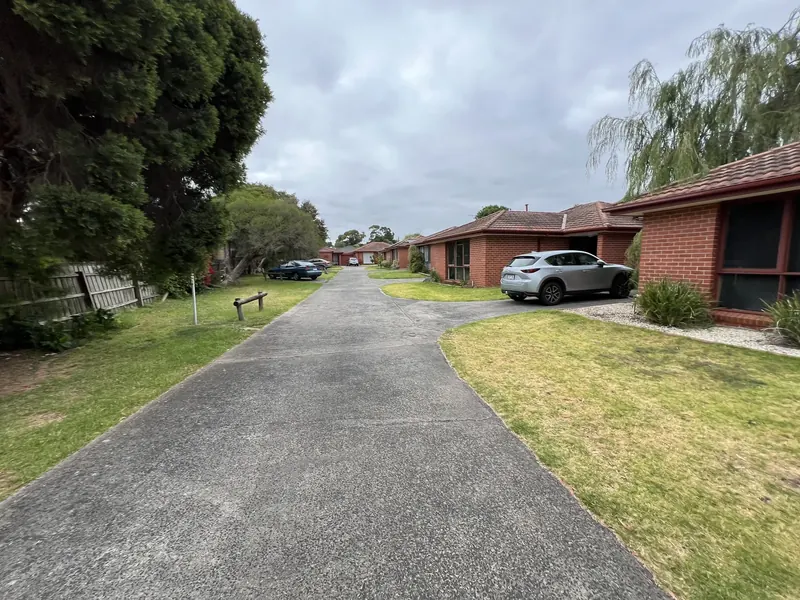 Established trees beside the shared driveway of a Frankston unit complex under an overcast sky